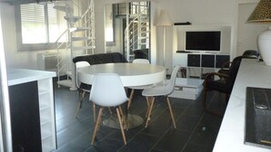 Ein modernes Wohnzimmer mit einem runden Esstisch, weißen Stühlen, einer Couch, einem Fernseher und einer Treppe.