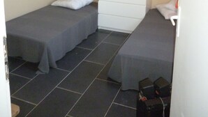 Ein kleines Zimmer mit zwei Einzelbetten, einer weißen Kommode und einem kleinen Tisch mit Lampe.