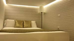 Un dormitorio con cama, paredes blancas y una pared de ladrillo.