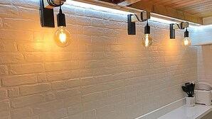 Una cocina con paredes de ladrillo blanco, encimera blanca y tres lámparas colgantes con bombillas expuestas.