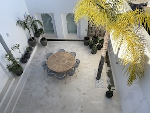 A patio area with a round table and chairs, surrounded by potted plants and a tiled floor.