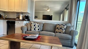 Eine moderne Küche mit weißen Schränken, einem grauen Sofa mit gemusterten Kissen, einem Holzesstisch und einer roten Ablagetasse.