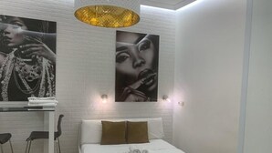 Un dormitorio moderno con una cama blanca, cabecera con dos almohadas, una mesita de noche con lámpara y dos sillas.