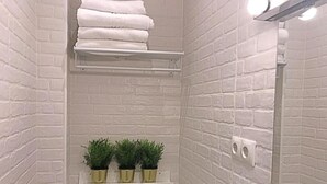 Un baño con paredes de ladrillo blanco, un inodoro, un estante con plantas y un perchero para toallas.