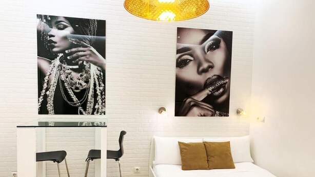 Habitación de hotel con una cama blanca, una mesita con dos sillas y dos obras de arte colgadas en la pared.