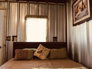 A bed with a wooden headboard, a window with a view of the outside, and a framed picture on the wall. - Pretty horse cabin in the woods (Willis)