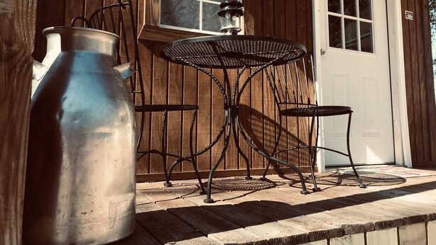 Une table et des chaises en métal, posées sur une terrasse en bois, avec un grand pot en métal et une lanterne.