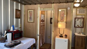 Une petite pièce comprenant un lit, un four à micro-ondes, un réfrigérateur et une porte donnant sur une autre pièce.
