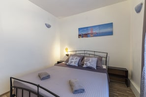 A neatly made bed with pillows and a folded towel, a bedside table with a lamp, and a painting of a bridge on the wall. - Apartment with a large terrace overlooking the pool. (FAŽANA)