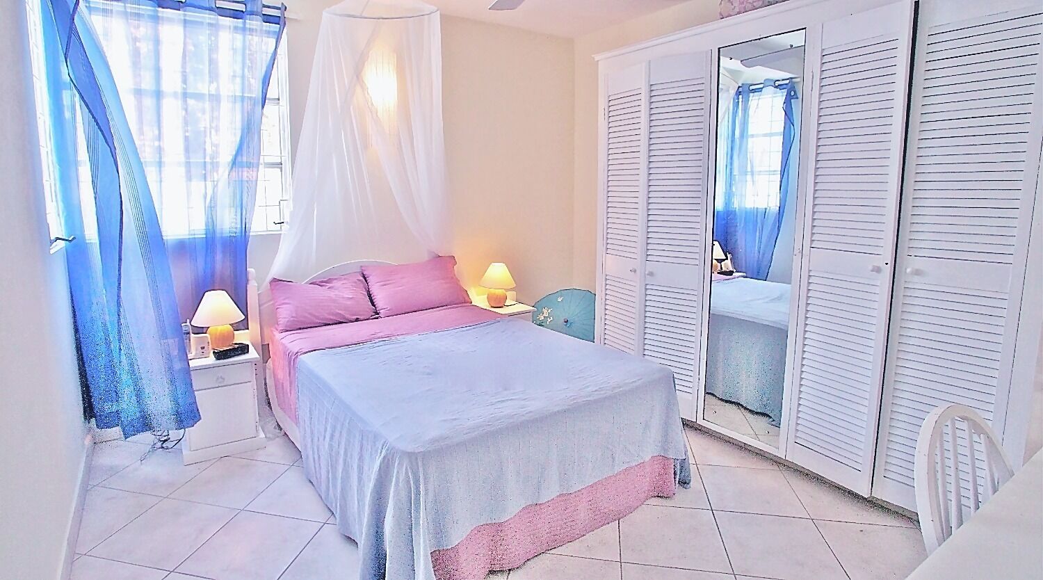 A bedroom with a bed, bedside lamps, a nightstand, a wardrobe, and a window with curtains.