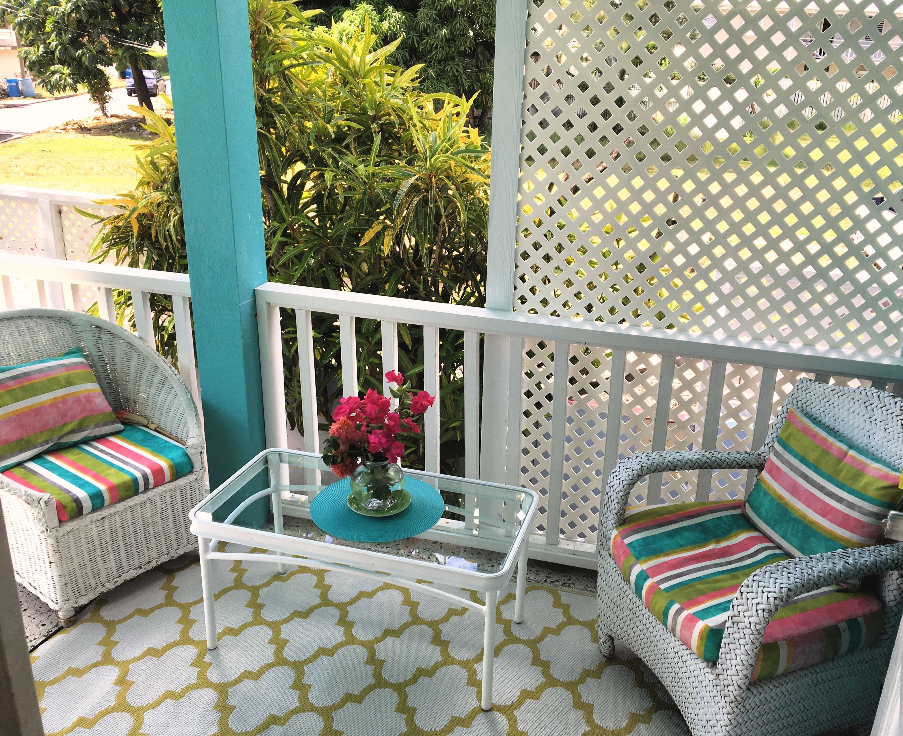 A balcony with wicker chairs, a glass table, and a decorative vase.