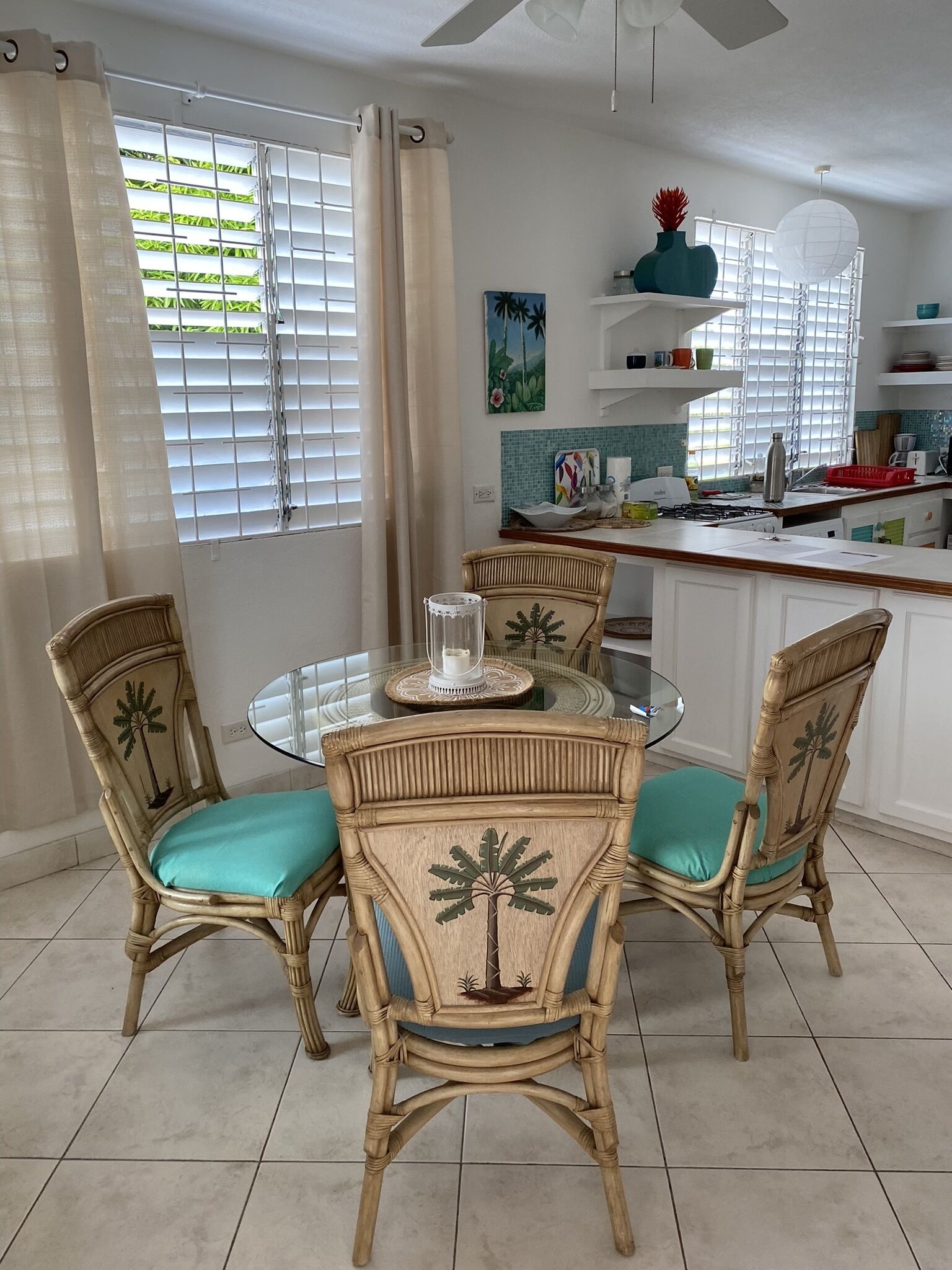 Un coin repas avec une table ronde en verre, entourée de quatre chaises en osier dotées de coussins turquoise.
