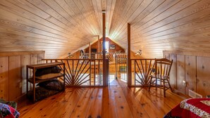 Un dormitorio de madera en el ático, con techo inclinado, una silla de madera, una mesita pequeña y vistas a través de una ventana.