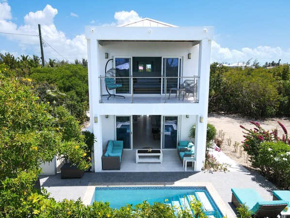 Una casa moderna de dos pisos con balcón, piscina y mobiliario exterior.