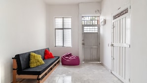 Un couloir avec un banc en bois, un pouf violet et une porte blanche dotée d’un portail en métal.