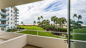A balcony with a view of a beach, palm trees, and a well-maintained lawn. - Beachfront efficiency studio with 1 bath (Marco Island)