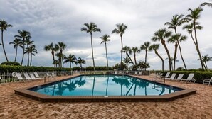 A rectangular pool with a brick border, surrounded by white lounge chairs and palm trees. - Beachfront efficiency studio with 1 bath (Marco Island)