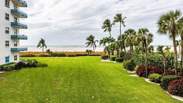 A well-maintained lawn, palm trees, and a building with balconies overlooking a beach. - Beachfront efficiency studio with 1 bath (Marco Island)
