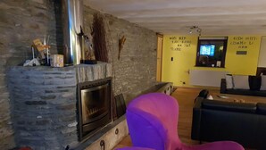 Un saló d'estar acollidor amb una llar de pedra, un televisor modern i seients confortables.