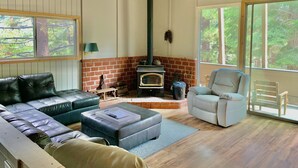 Una sala de estar acogedora con chimenea de ladrillo, un sofá, un sillón y amplios ventanales con vistas al exterior.