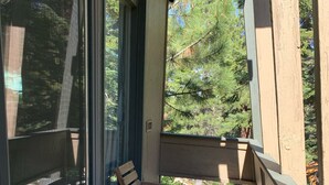 Una terraza de madera con dos sillas y una pequeña mesa, con vista a un área boscosa.