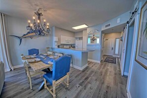 A dining area with a wooden table and blue chairs, a kitchen with white cabinets, and a chandelier. - Shores of Panama 1529-End Unit~Sleeps 8 (Panama City Beach)