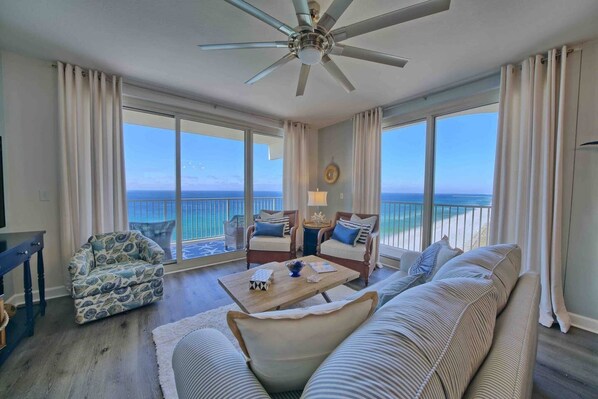 A spacious living room with a large window offering a view of the ocean, a ceiling fan, and a cozy seating area with a coffee table. - Shores of Panama 1529-End Unit~Sleeps 8 (Panama City Beach)
