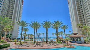 A resort pool area with palm trees, lounge chairs, and a view of the ocean. - Shores of Panama 1529-End Unit~Sleeps 8 (Panama City Beach)