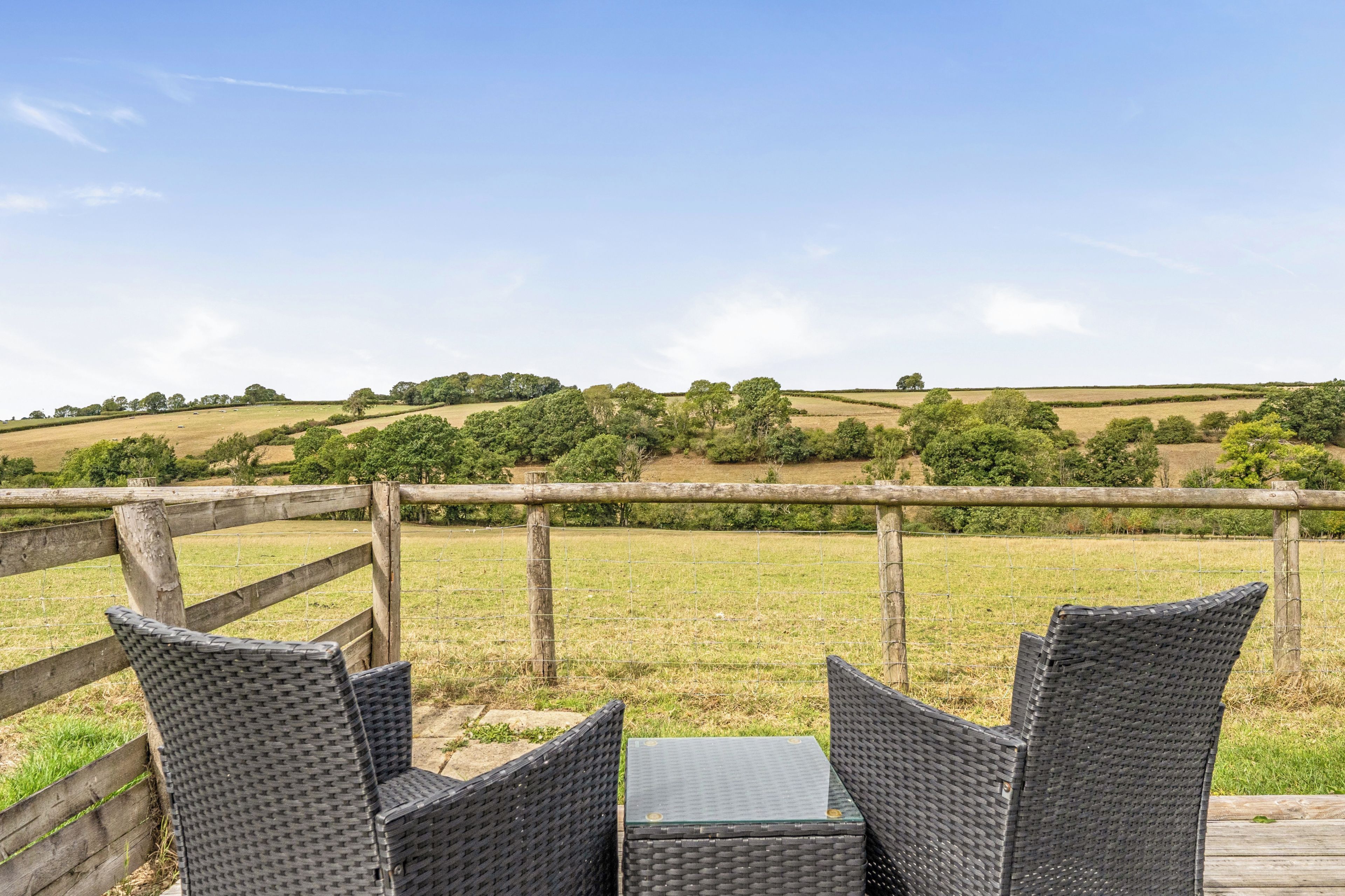 A wicker table and chairs set outdoors with a view of rolling hills and trees.