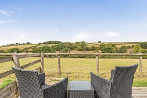 A wicker table and chairs set outdoors with a view of rolling hills and trees. - The Shippon, Breathtaking Views, Private Hot Tub (Winkleigh)
