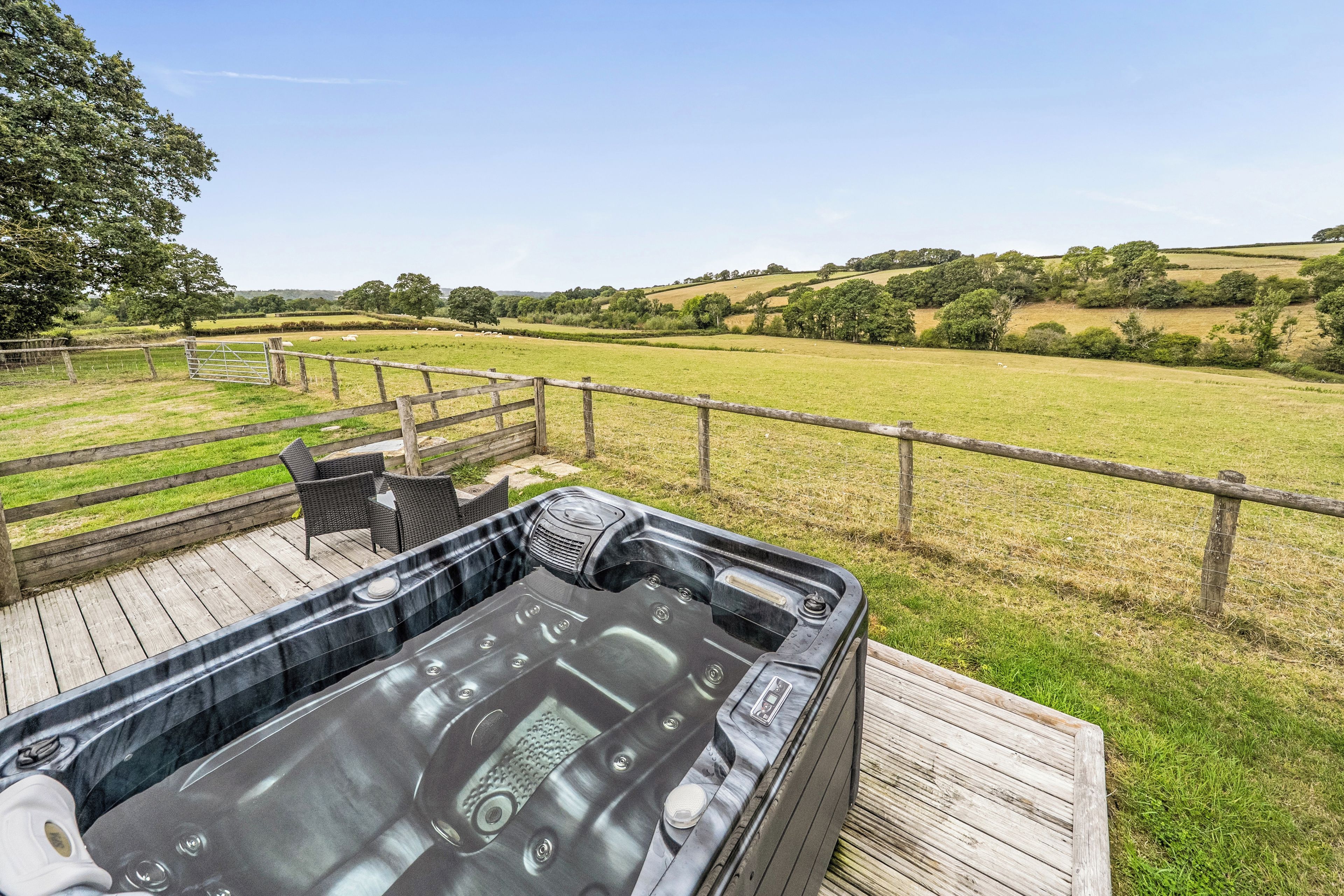 A hot tub on a wooden deck with a view of a grassy field and hills.