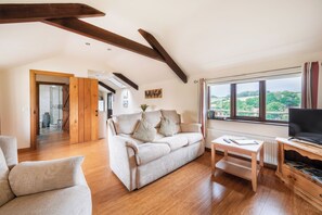 Un salon spacieux doté d’un plancher en bois, d’un canapé, d’une table basse et d’un téléviseur posé sur un meuble en bois.