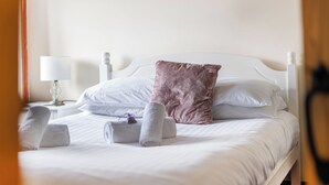 A neatly made bed with white linens and a single pink pillow, accompanied by rolled towels on the side. - The Shippon, Breathtaking Views, Private Hot Tub (Winkleigh)
