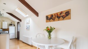 A dining area with a white table and chairs, a vase with flowers, and a wooden rooster painting on the wall. - The Shippon, Breathtaking Views, Private Hot Tub (Winkleigh)