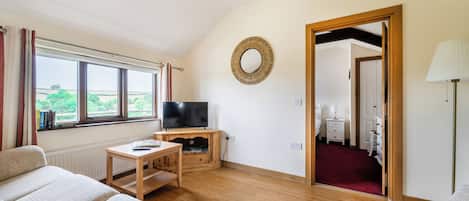 A living room with a television, wooden furniture, a large window, and a view of greenery outside.