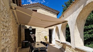 A stone building with a covered patio, outdoor seating, and a view of the surrounding landscape. - 🏡 Spacious, air-conditioned 8-person gîte with swimming pool, between history, nature and the sea (Sommières)