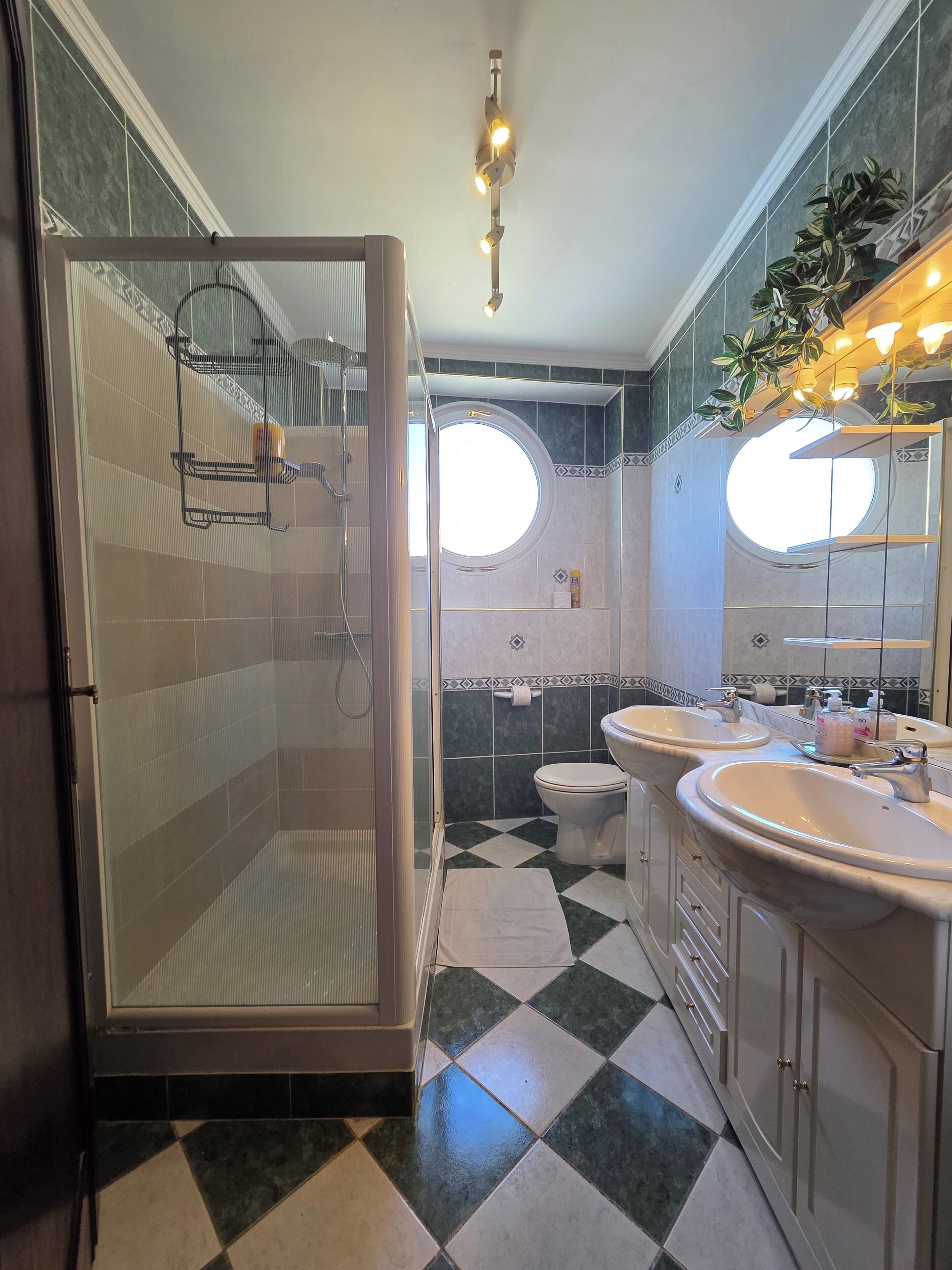 Et badeværelse med bruser, to håndvaske, toilet og et stort spejl.