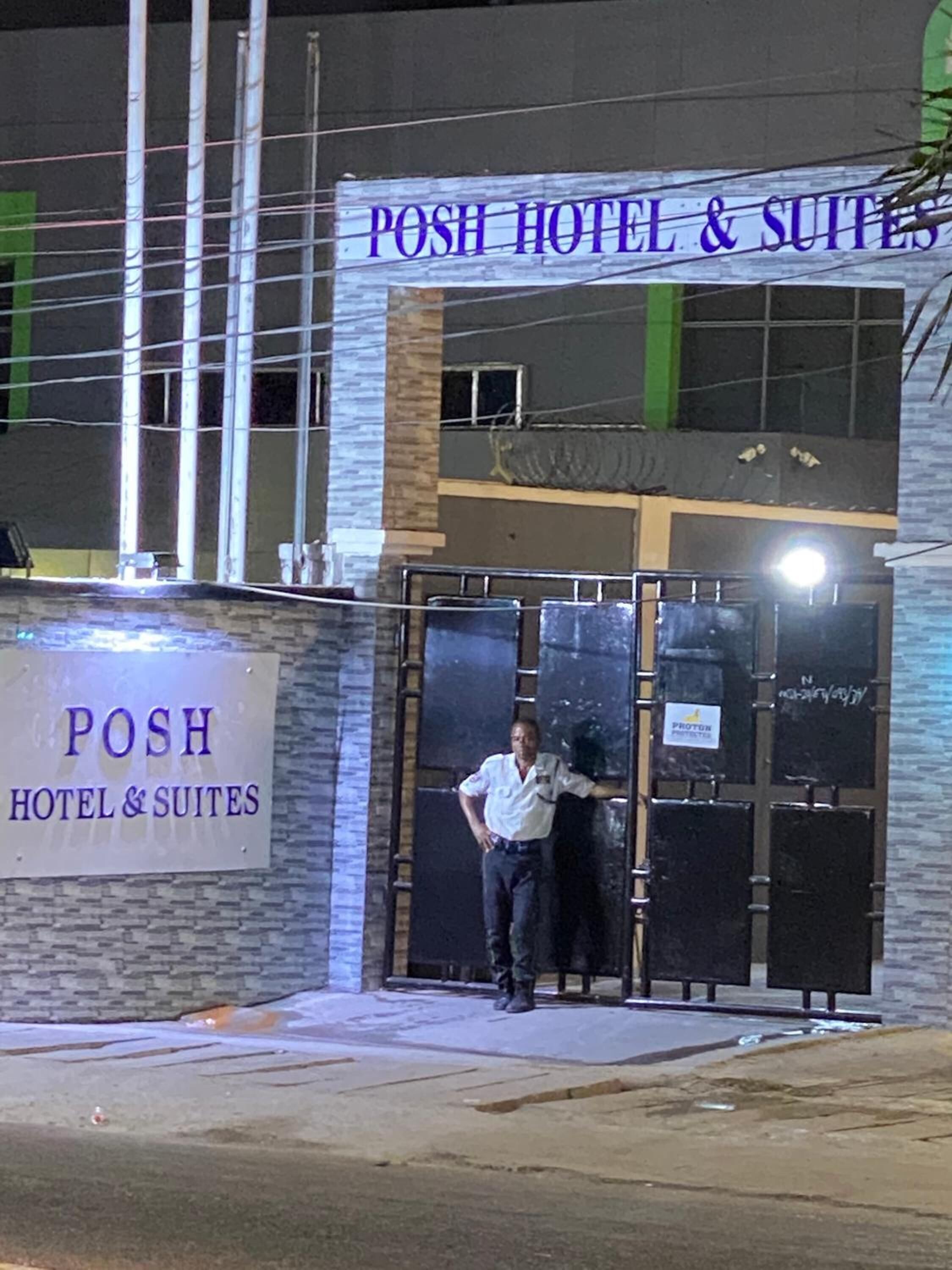 A hotel entrance with a sign reading "POSH HOTEL & SUITES" and a security guard standing by the door.