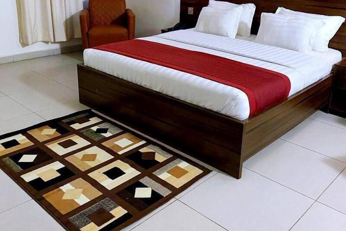 A neatly made bed with a wooden headboard, a red blanket, and a patterned rug.