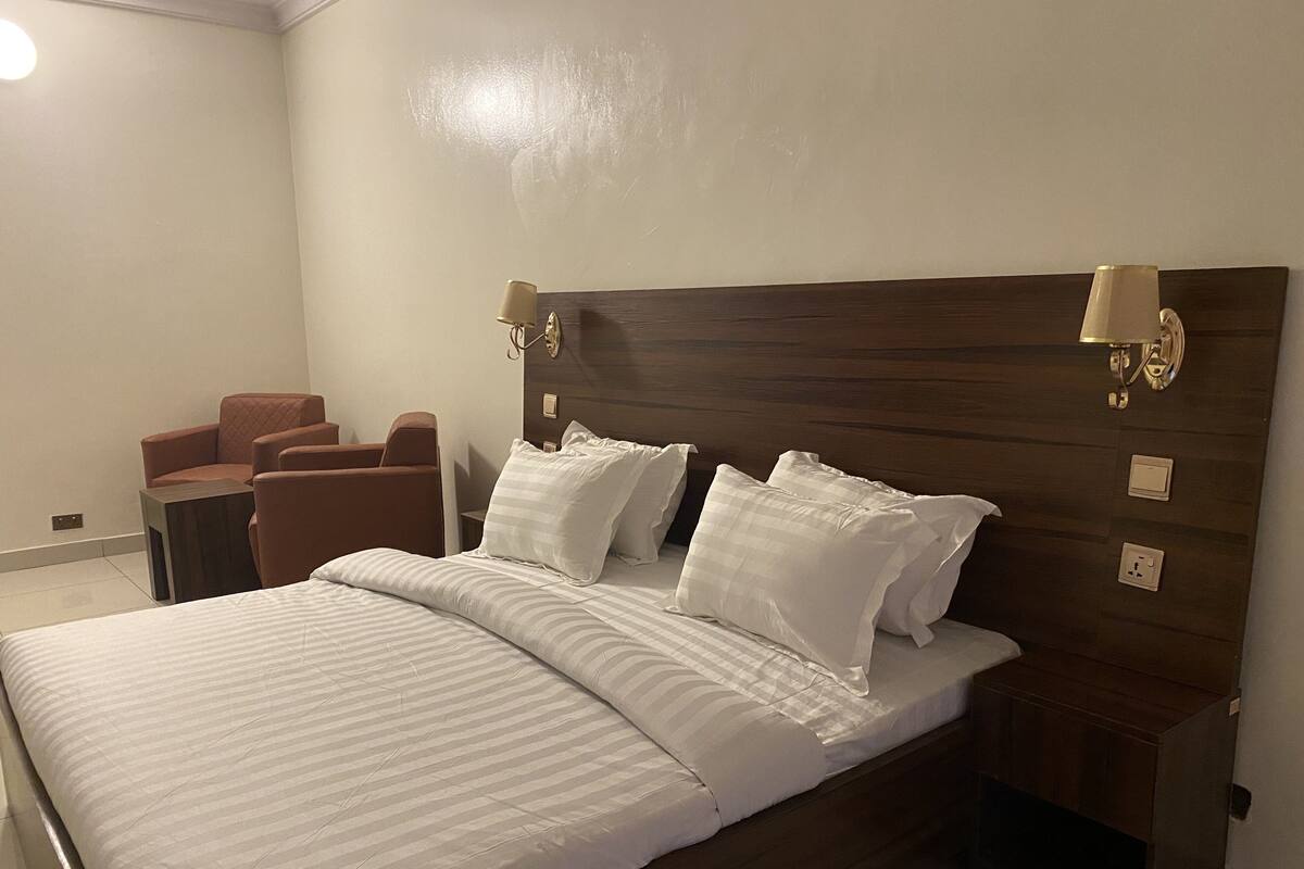 A neatly made bed with white linens and a wooden headboard, accompanied by two bedside lamps and a small nightstand.