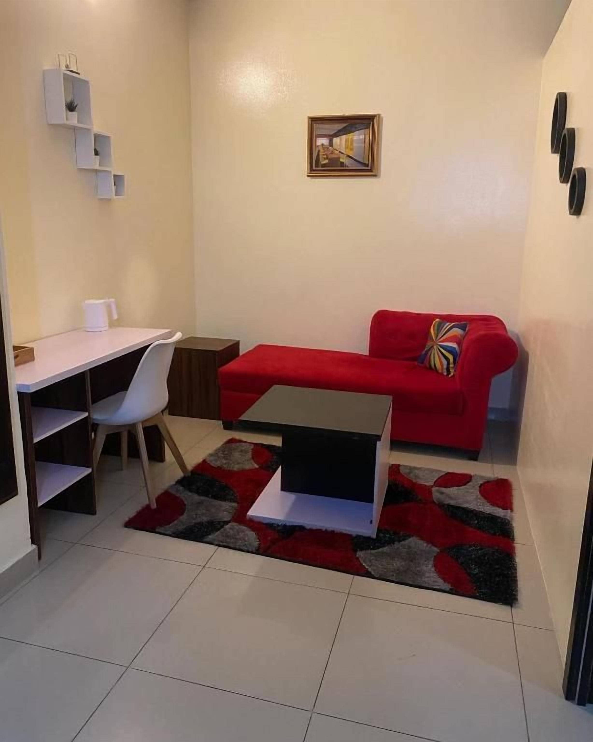 A compact living space with a red sofa, a small table, a white chair, and a desk.