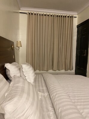 Habitació d'hotel amb un llit gran, dos almoinos, un capçal de llit, una làmpada penjant a la paret i una finestra amb cortines.