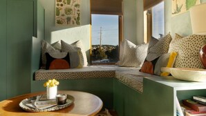 Una habitación acogedora con una zona de estar con bancos, una ventana con vistas y una pequeña mesa con un florero.