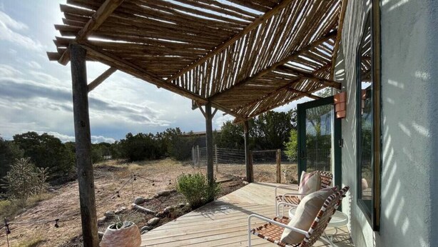 Una terraza de madera con dos sillas de mimbre, una jardinera de piedra y una estructura de pérgola.