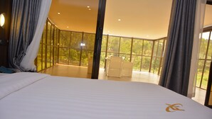 A spacious bedroom with a large bed, a balcony with a view of greenery, and a seating area with a chair. - FK Resort & Spa (Marua)