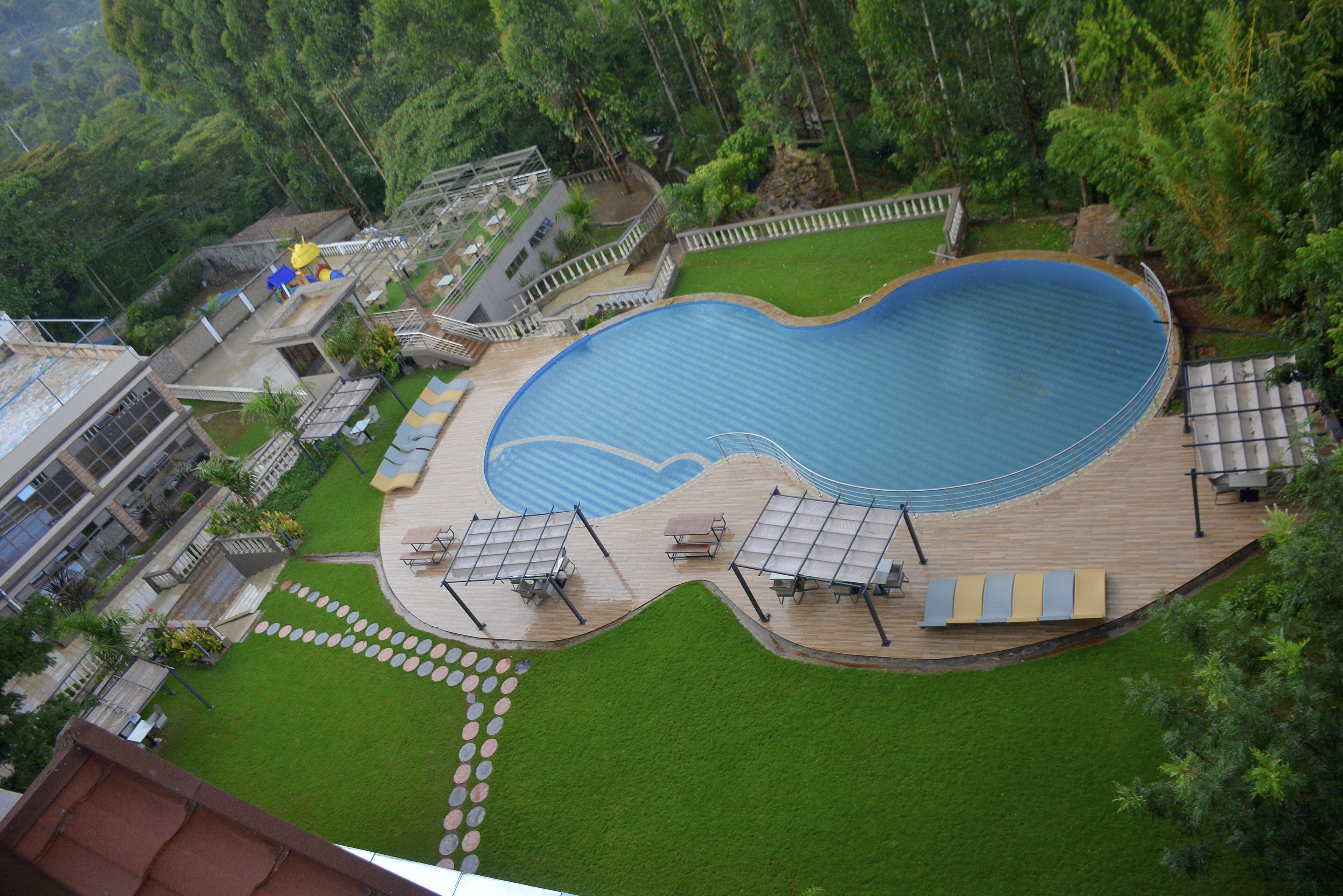 An aerial view of a resort with a large swimming pool, sun loungers, and a well-maintained lawn.