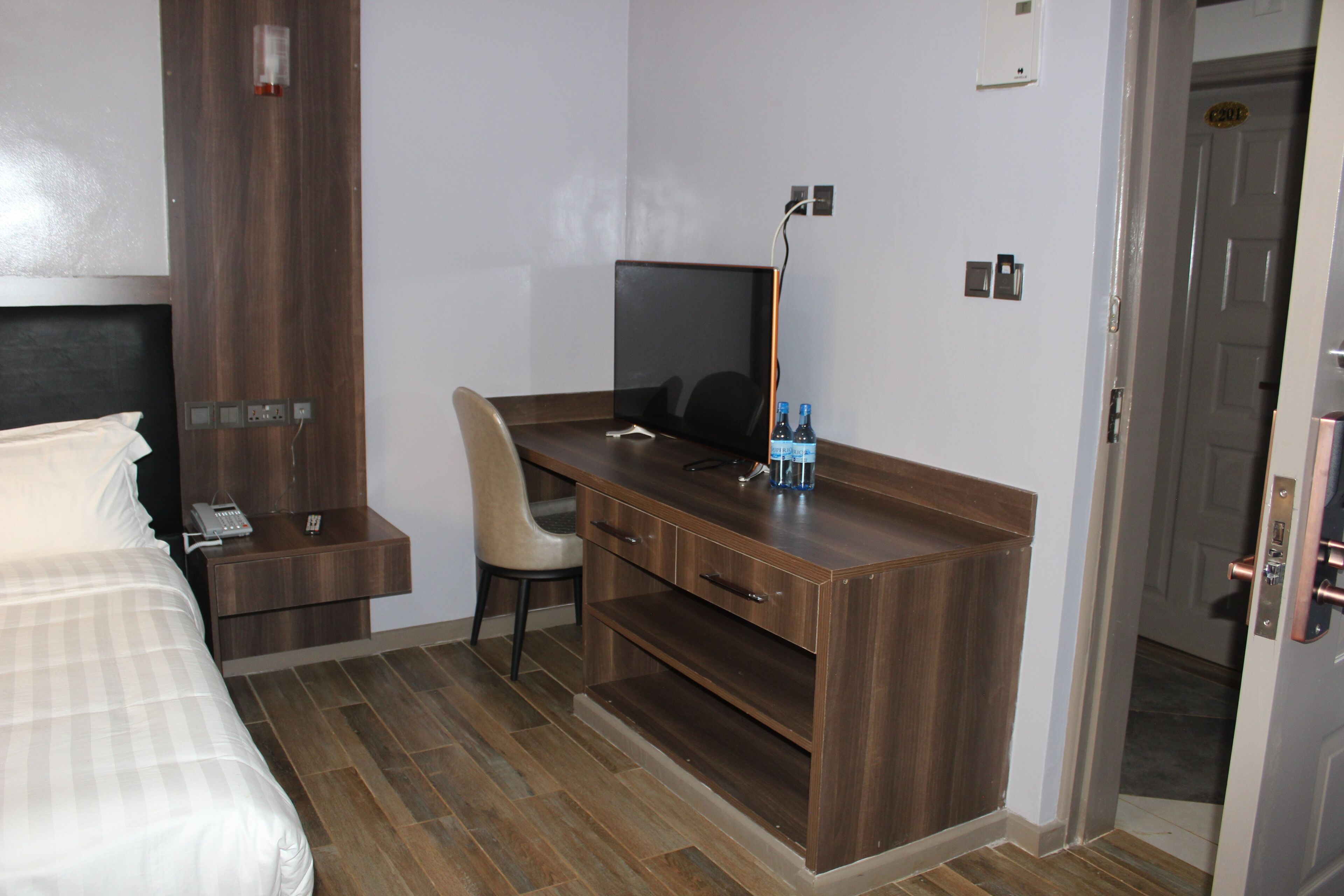 A hotel room with a bed, a desk with a chair, a television, and a minibar.