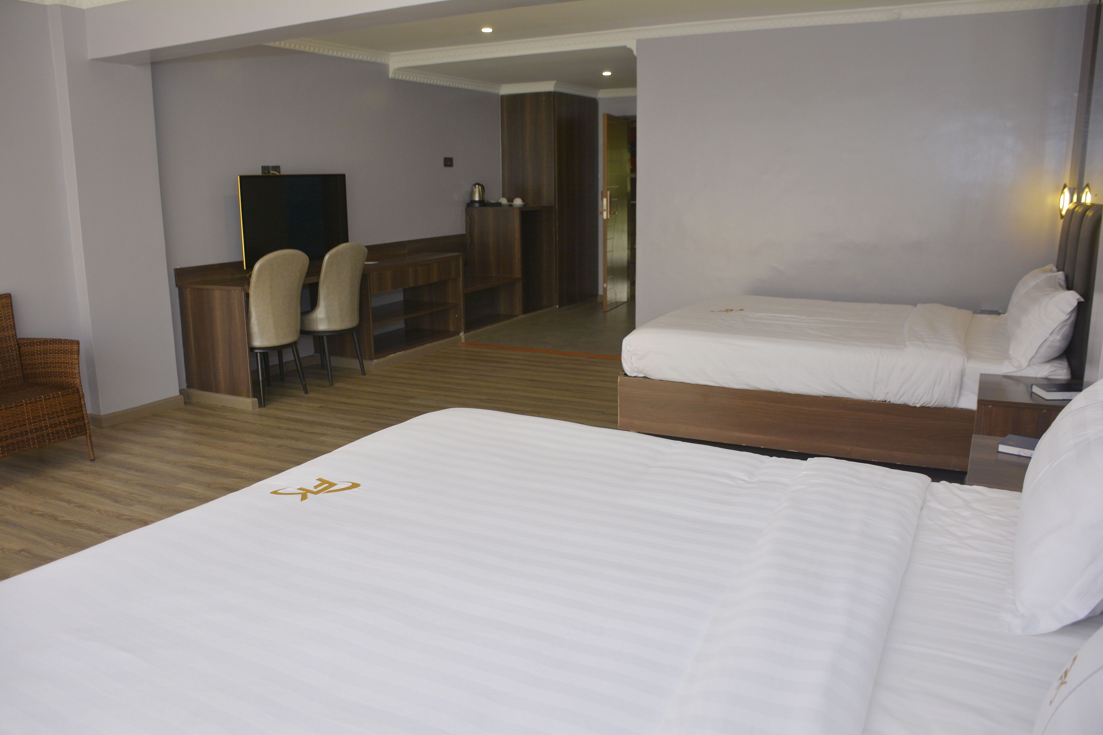 A hotel room with two beds, a desk with chairs, and a television.