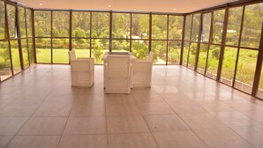 A spacious room with large windows offering a view of a lush garden. There is a table with chairs in the center. - FK Resort & Spa (Marua)