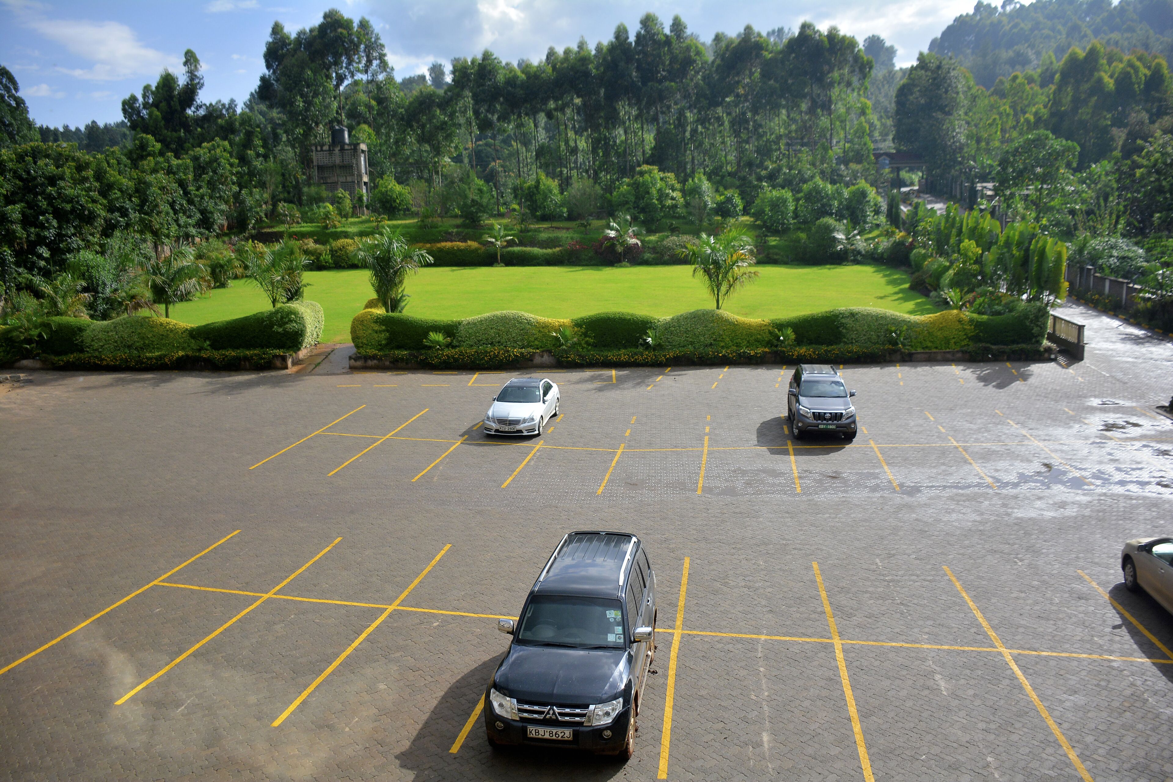A parking lot with three cars and a lush green landscape in the background.